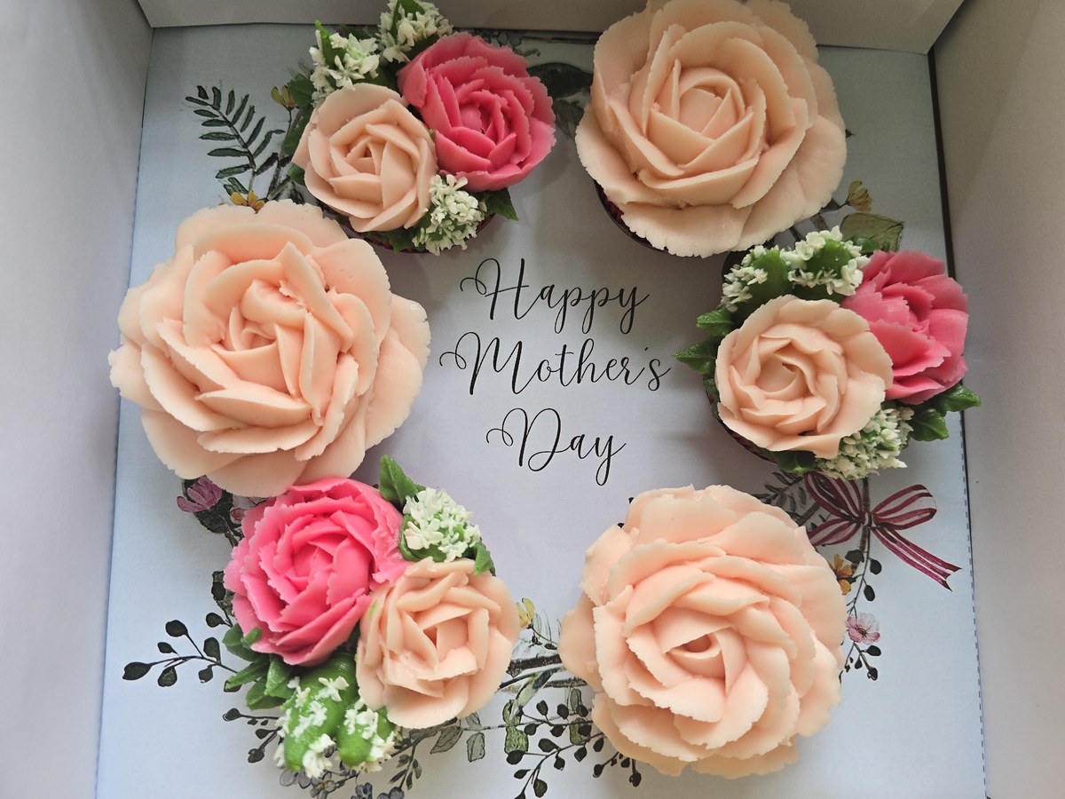 Peach and pink buttercream floral cupcakes arranged around a Mother's Day message