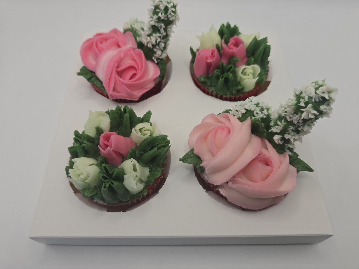 Four pink, ivory and green buttercream floral cupcakes on a white presentation insert