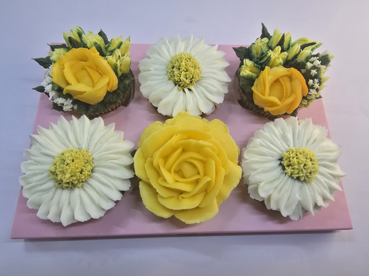 Six yellow and ivory buttercream floral cupcakes on a pale presentation insert